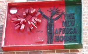 Red and green artword by Joe Sam, saying "the New Africa House" mounted on brick.