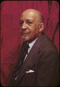 W.E.B. Du Bois, seated against a red backdrop