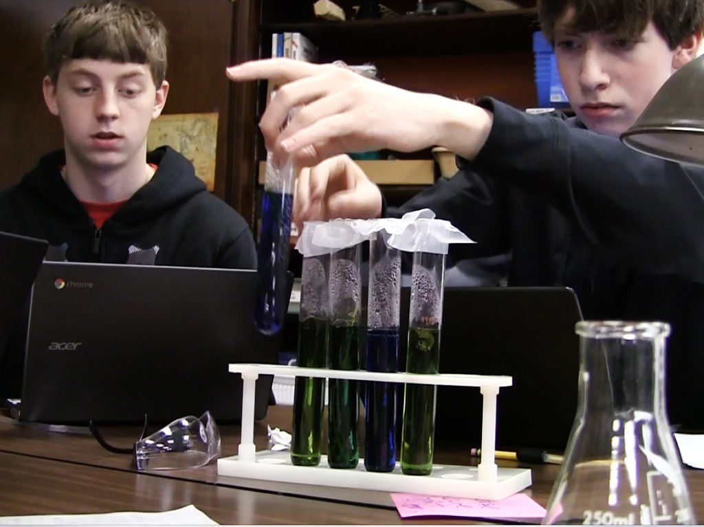 Two male high school students collaborating on a science experiment.