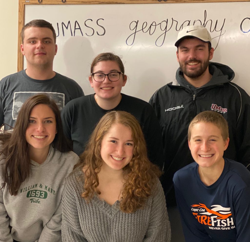 The six Geography Club E-Board representatives pose in two rows in front of a white board at their first meeting of the semester.